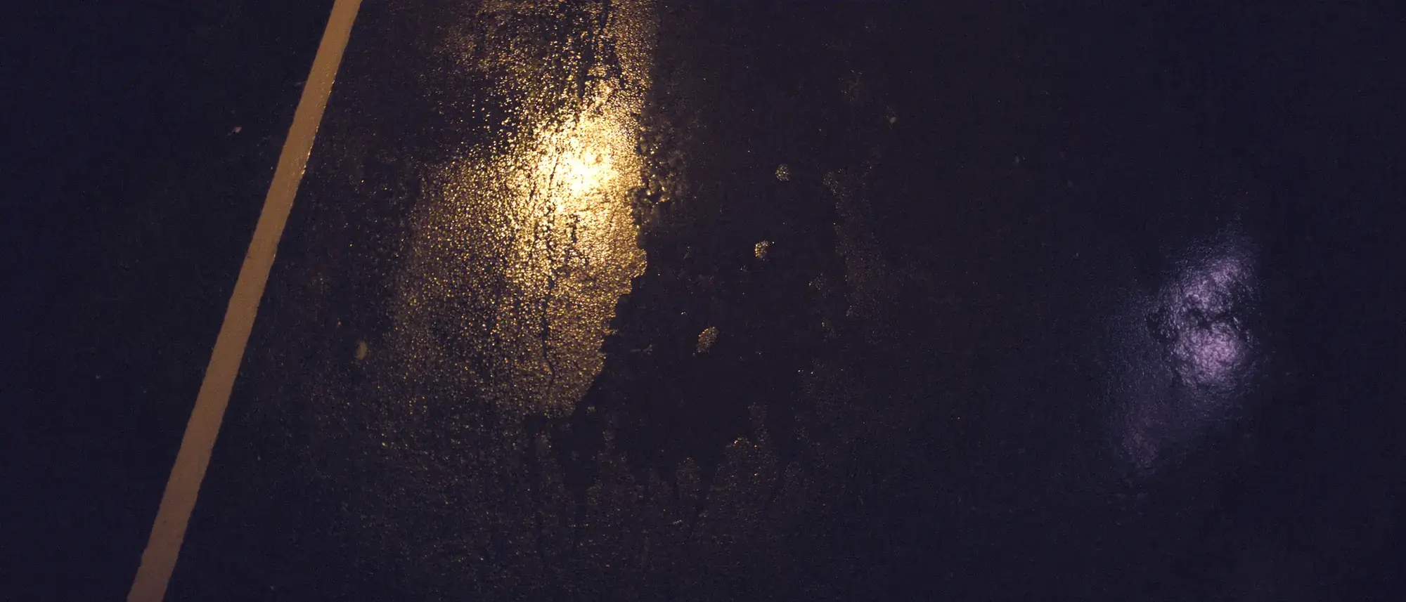 Wet night asphalt with smeared street-lamp reflections and worn lane paint