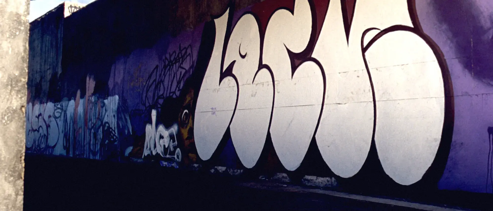 A concrete wall covered in bold abstract graffiti in violet and bone white