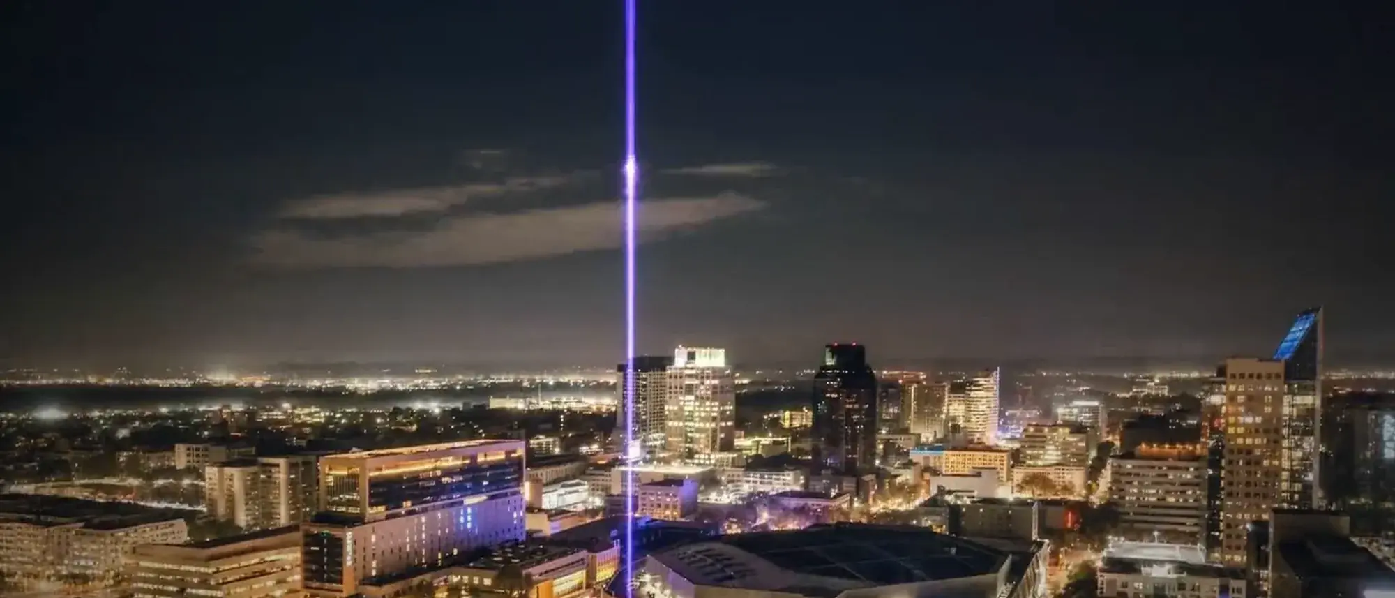 The downtown Sacramento skyline at night under a violet beam standing over the city