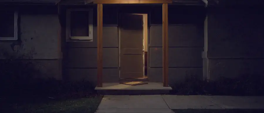 A plain door ajar at night with warm light falling across the step
